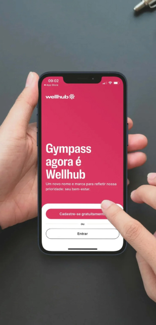 Mão segurando um smartphone segurando o app da Wellhub, com a frase: Gympass agora é Wellhub